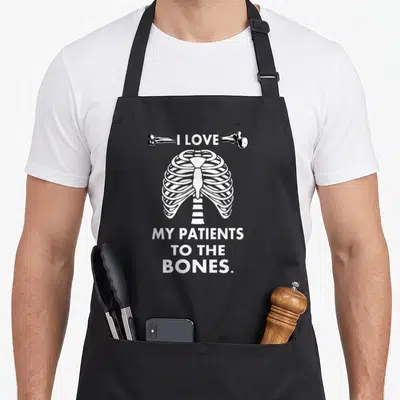 Chiropractor patient apron - White ribcage graphic with I LOVE MY PATIENTS TO THE BONES text flanked by two bones — shown on a black cotton canvas apron against a white background