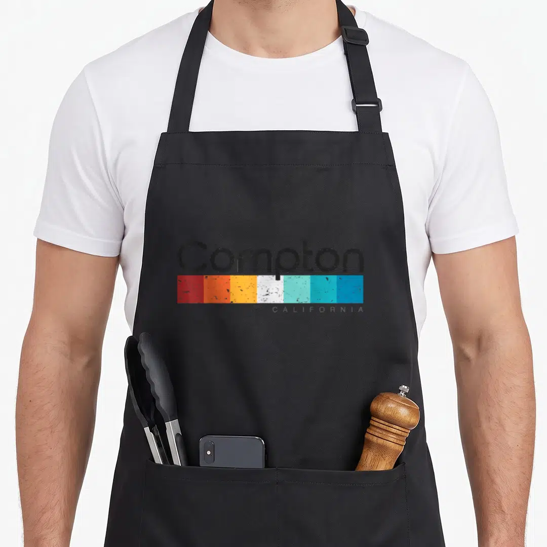 Vintage california compton apron - Compton text above seven distressed color blocks in red, orange, yellow, white — shown on a black cotton canvas apron against a white background