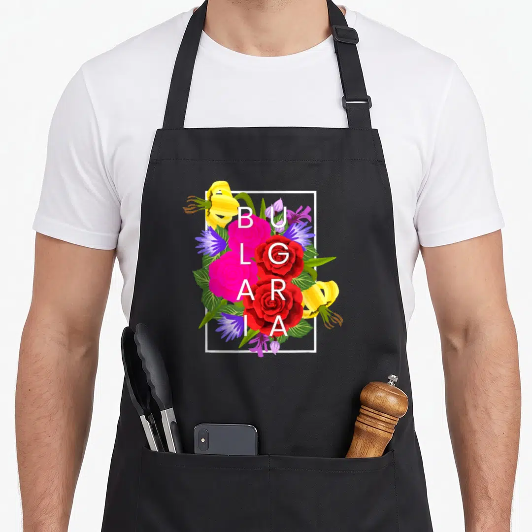 Bulgarian pride apron - Vertical BULGARIA text surrounded by red pink yellow and green flowers in a white frame — shown on a black cotton canvas apron against a white background