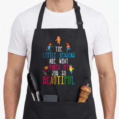 Reason daycare teacher aprons - Stacked text The Little Reasons Makes My Job So Beautiful surrounded by four running — shown on a black cotton canvas apron against a white background