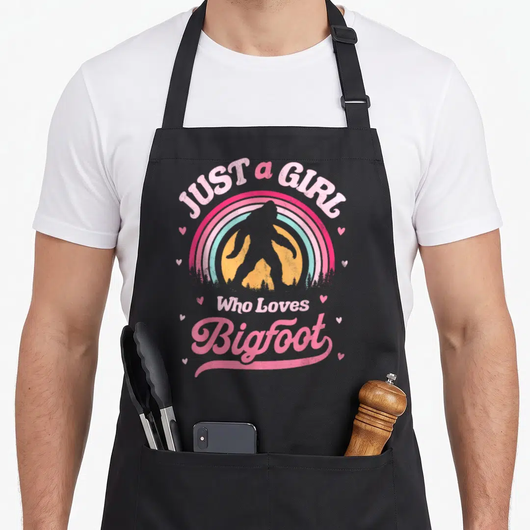 Funny sasquatch bigfoot apron - Retro rainbow with Bigfoot silhouette and pink text JUST a GIRL Who Loves Bigfoot — shown on a black cotton canvas apron against a white background