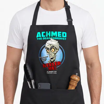 Achmed albany apron - Cartoon skeleton head with teal text ACHMED and red KEELED ME speech bubble — shown on a black cotton canvas apron against a white background