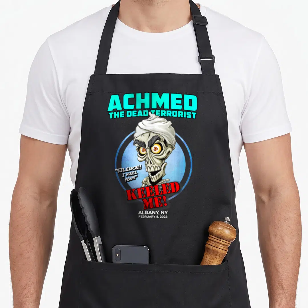 Achmed albany apron - Cartoon skeleton head with teal text ACHMED and red KEELED ME speech bubble — shown on a black cotton canvas apron against a white background