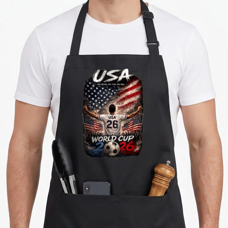 Cup football apron - Soccer player back view USA flag 2026 World Cup text red white blue — shown on a black cotton canvas apron against a white background