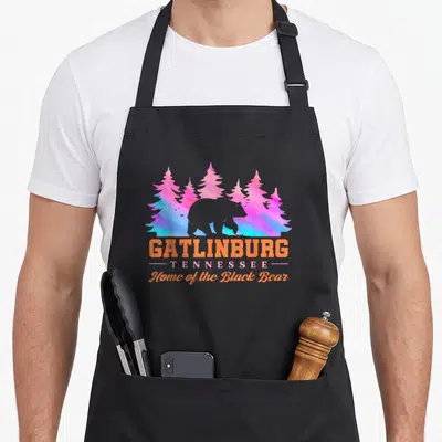 Gatlinburg tennessee bear apron - Dark grey bear silhouette against colorful pine trees with Gatlinburg Tennessee text — shown on a black cotton canvas apron against a white background