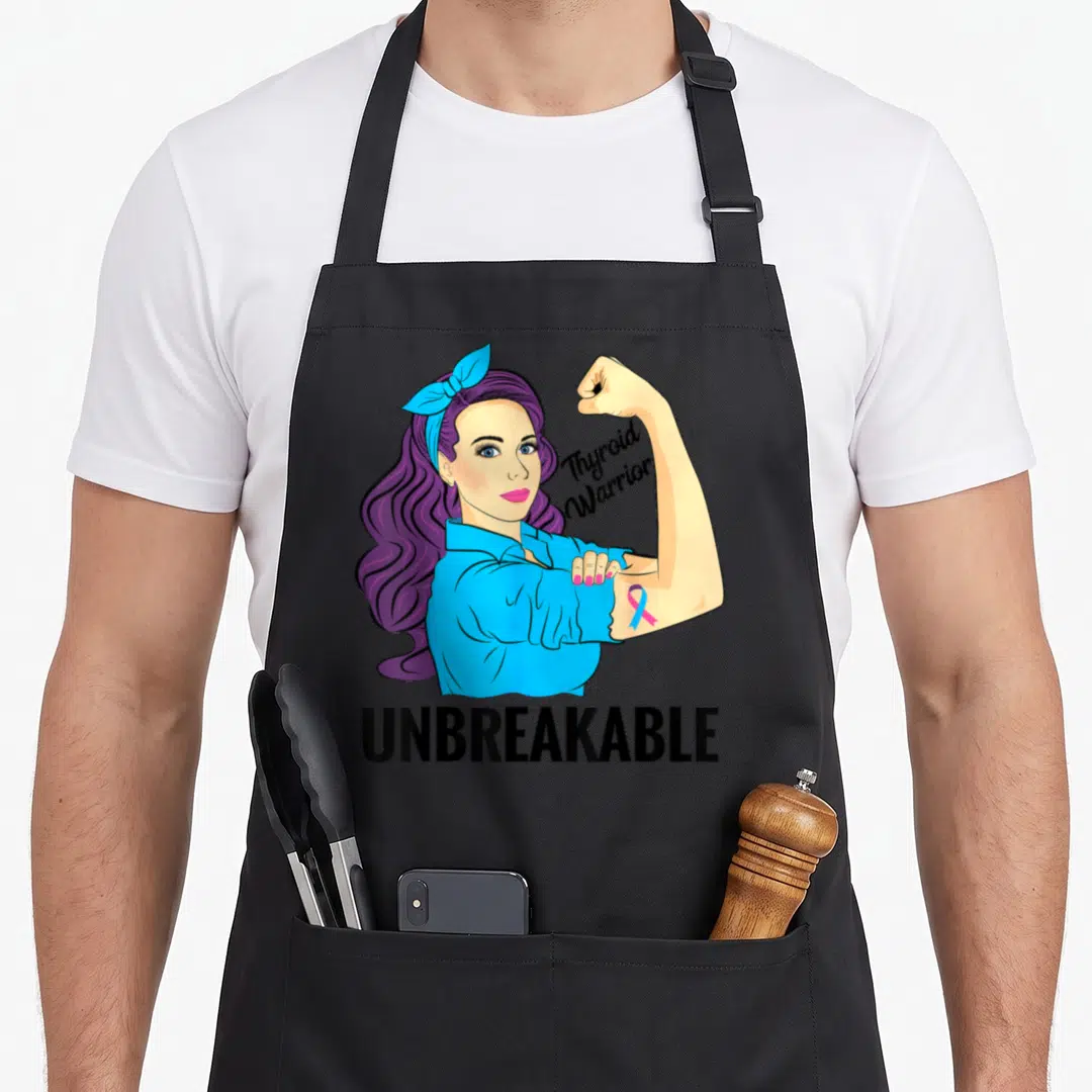 Unbreakable thyroid apron - Cartoon woman flexing arm with Thyroid Warrior script and UNBREAKABLE text in blue purple — shown on a black cotton canvas apron against a white background