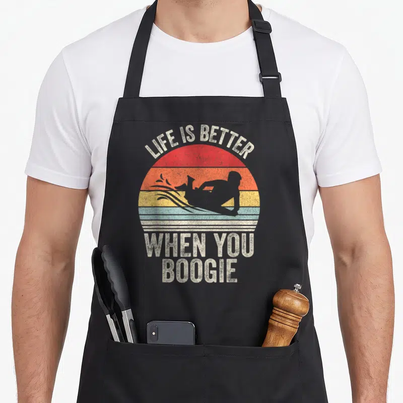 Ray crew apron - Retro striped sun with boogie boarder silhouette and LIFE IS BETTER WHEN YOU BOOGIE text — shown on a black cotton canvas apron against a white background