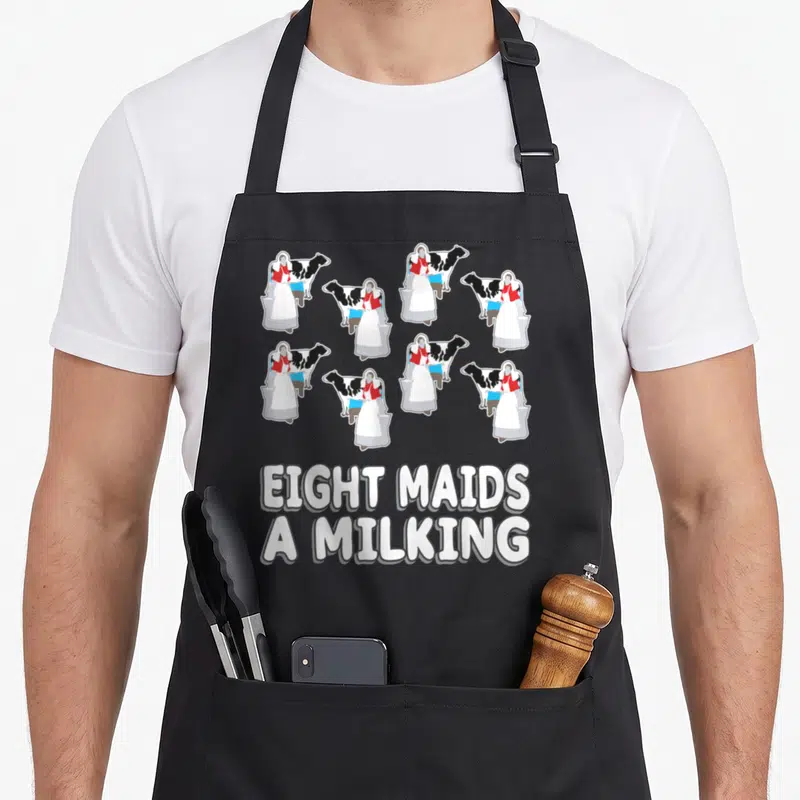 Maid christmas apron - Eight cartoon maids milking cows with stacked white text on grey background — shown on a black cotton canvas apron against a white background