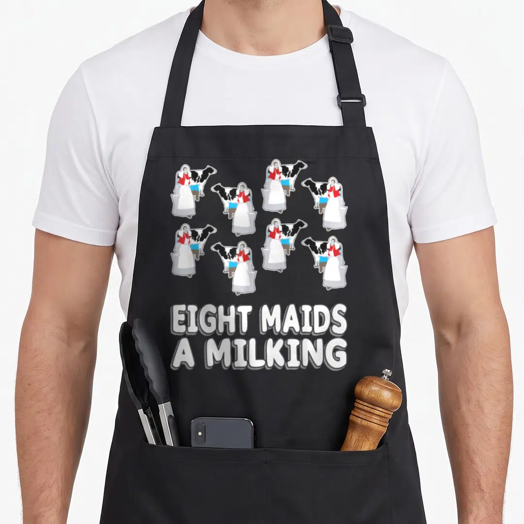 Maid christmas apron - Eight cartoon maids milking cows with stacked white text on grey background — shown on a black cotton canvas apron against a white background