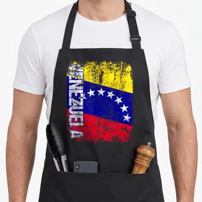 Venezuela distressed apron - Vertical VENEZUELA text over distressed yellow blue and red flag with white stars — shown on a black cotton canvas apron against a white background