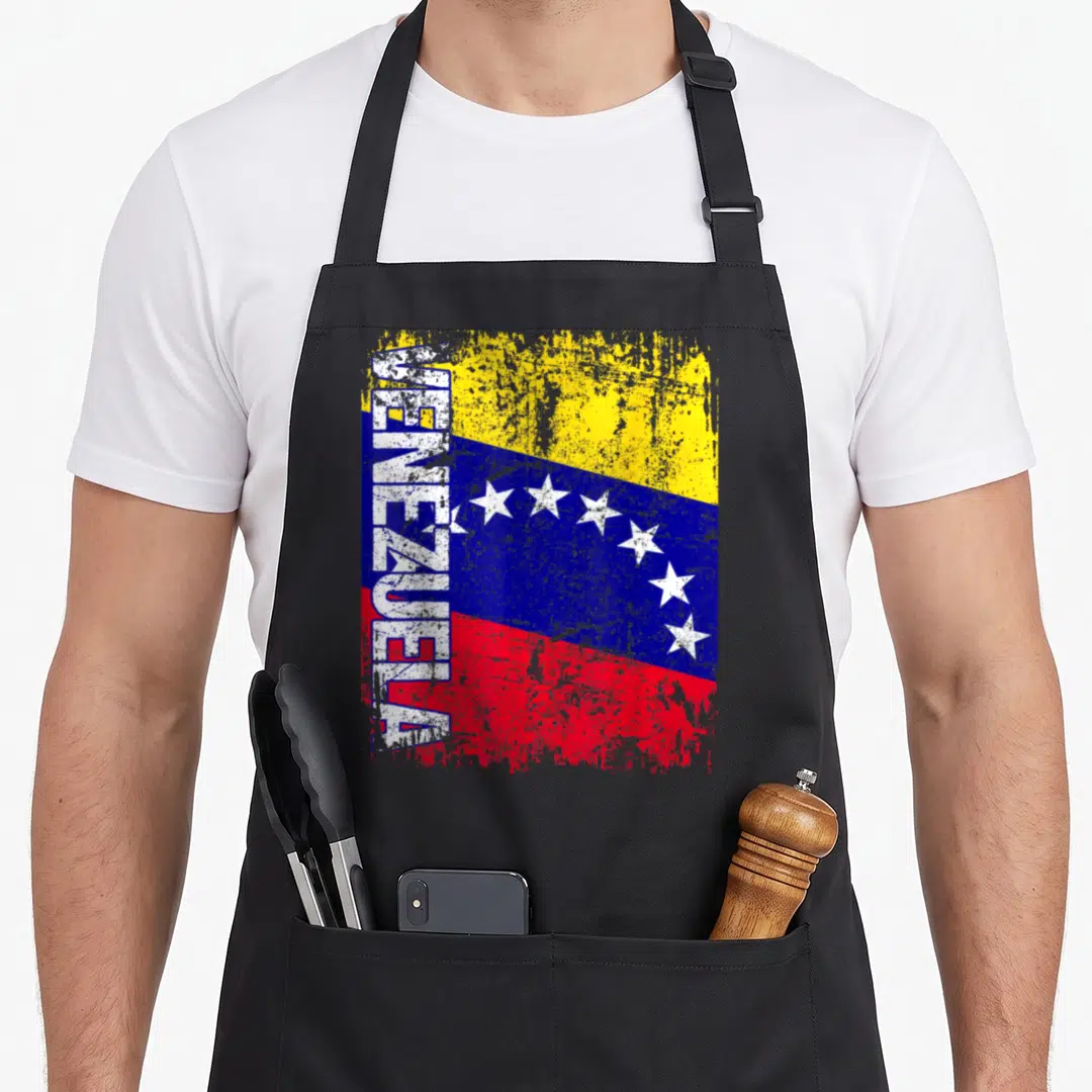 Venezuela distressed apron - Vertical VENEZUELA text over distressed yellow blue and red flag with white stars — shown on a black cotton canvas apron against a white background