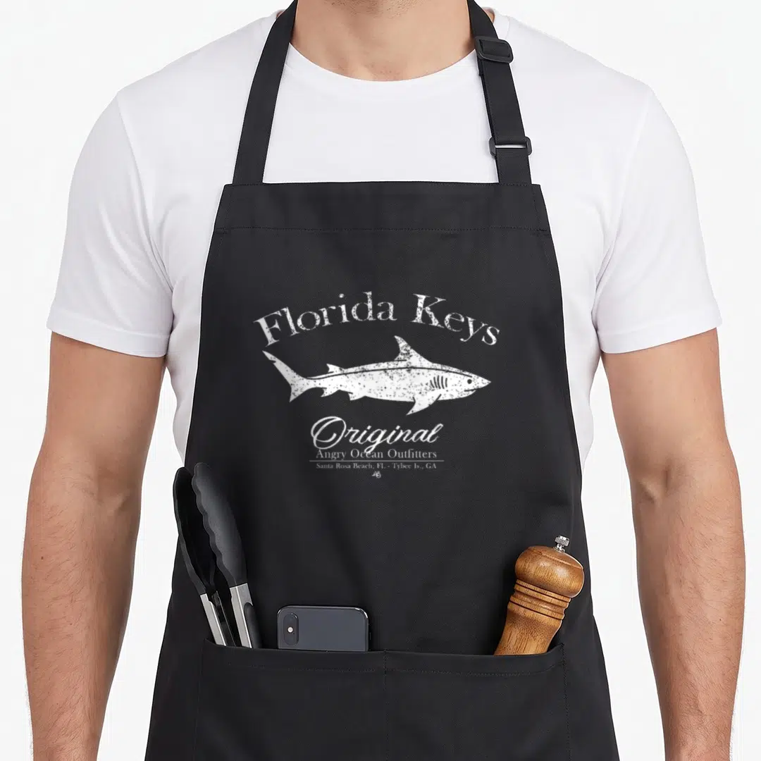 Shark florida apron - White distressed shark with Florida Keys text and Anger Ocean Outfitters label — shown on a black cotton canvas apron against a white background