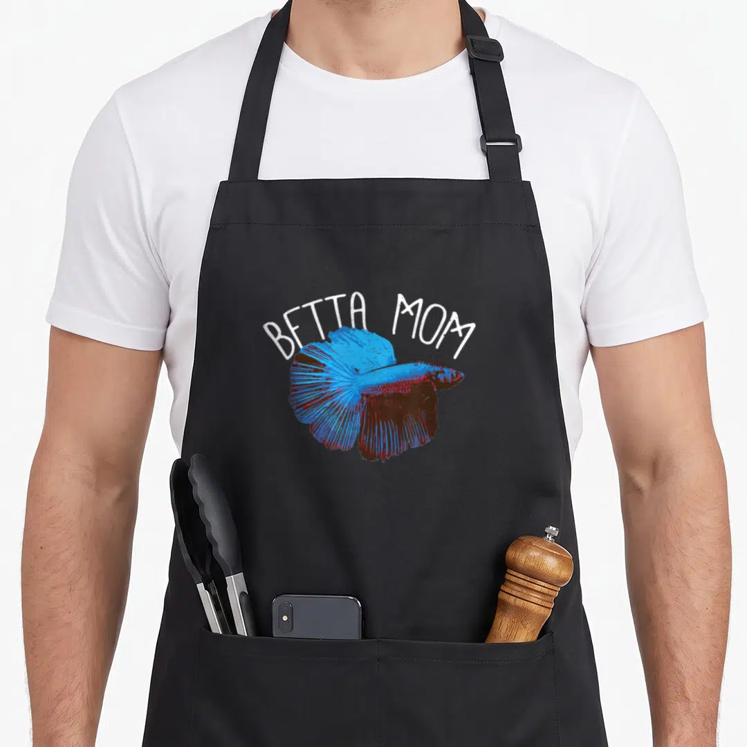 Fishkeeping mother's apron - Arched white BETTA MOM text above a blue and red cartoon betta fish illustration — shown on a black cotton canvas apron against a white background