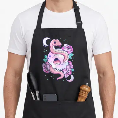 Scary goth apron - Pink snake coiled around white skull with roses and moons in cartoon style — shown on a black cotton canvas apron against a white background