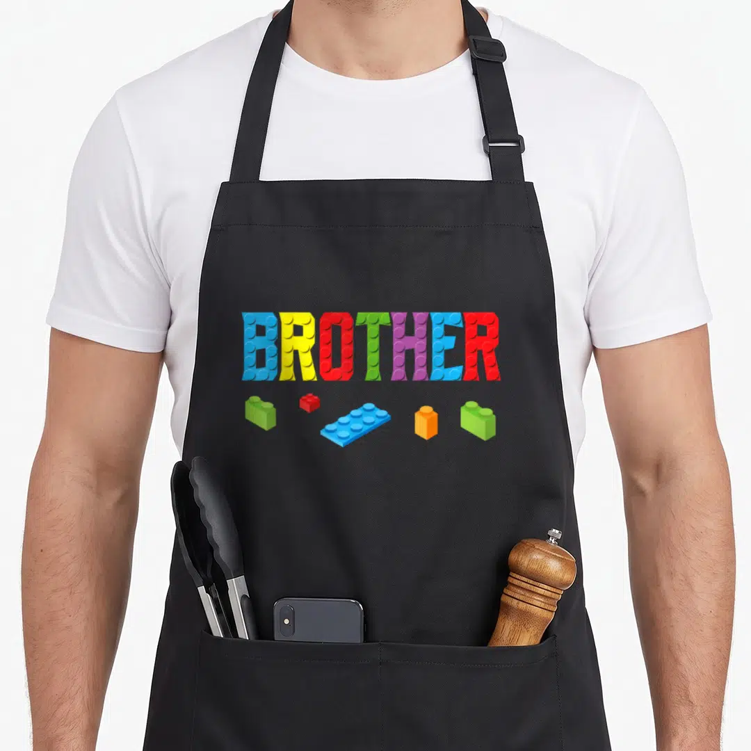 Family grill master apron - BROTHER text made of blue yellow red green purple orange toy bricks with five loose blocks — shown on a black cotton canvas apron against a white background