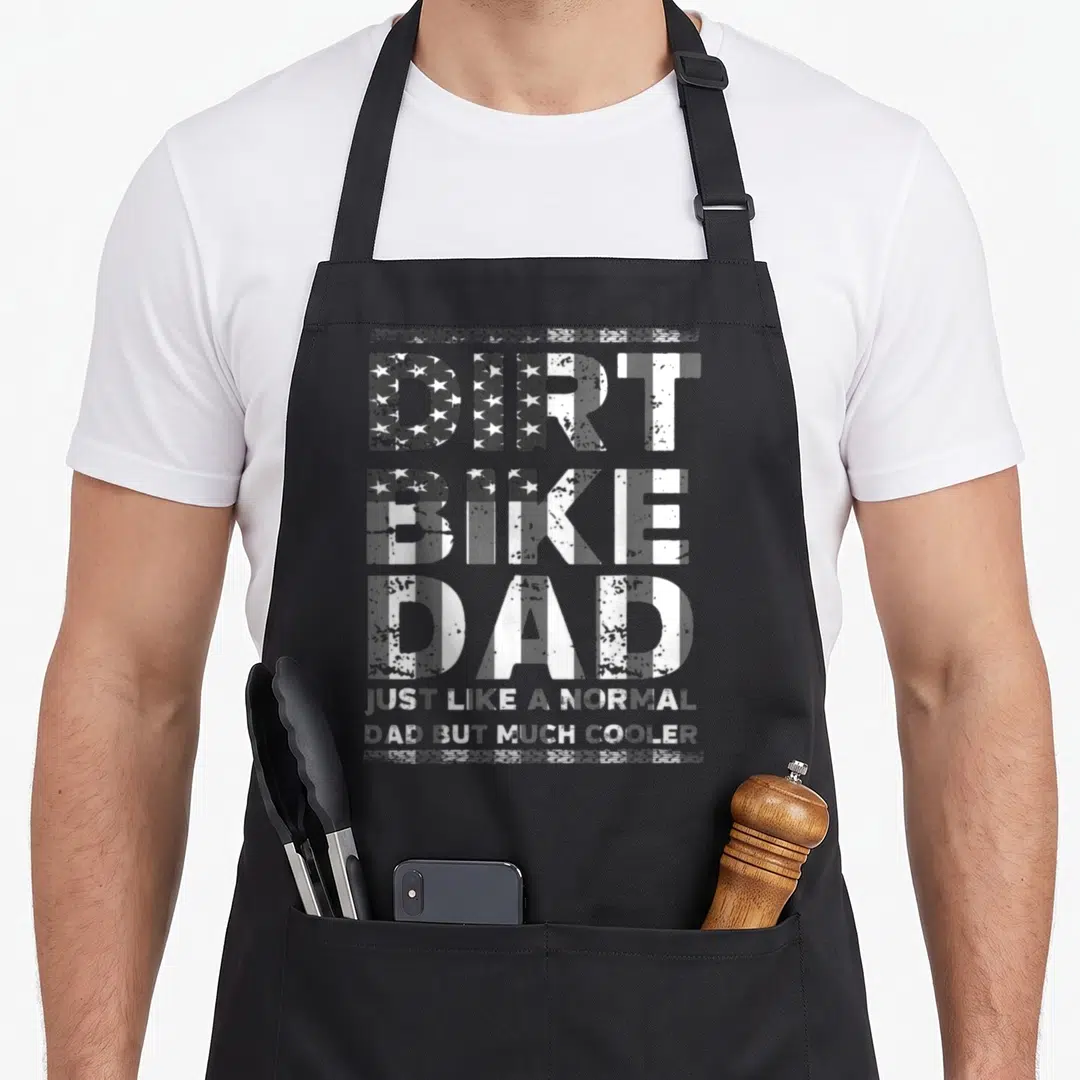 Flag bike apron - Distressed white and grey text reading DIRT BIKE DAD with flag pattern fill on three lines — shown on a black cotton canvas apron against a white background