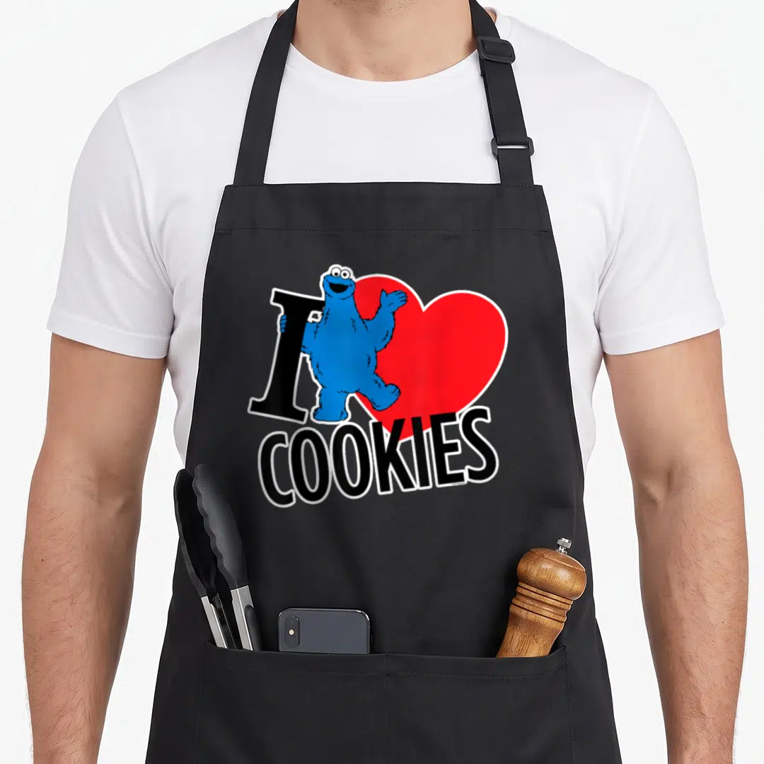 Funny cookie cookies apron - Blue character standing over red heart next to black I and COOKIES text — shown on a black cotton canvas apron against a white background