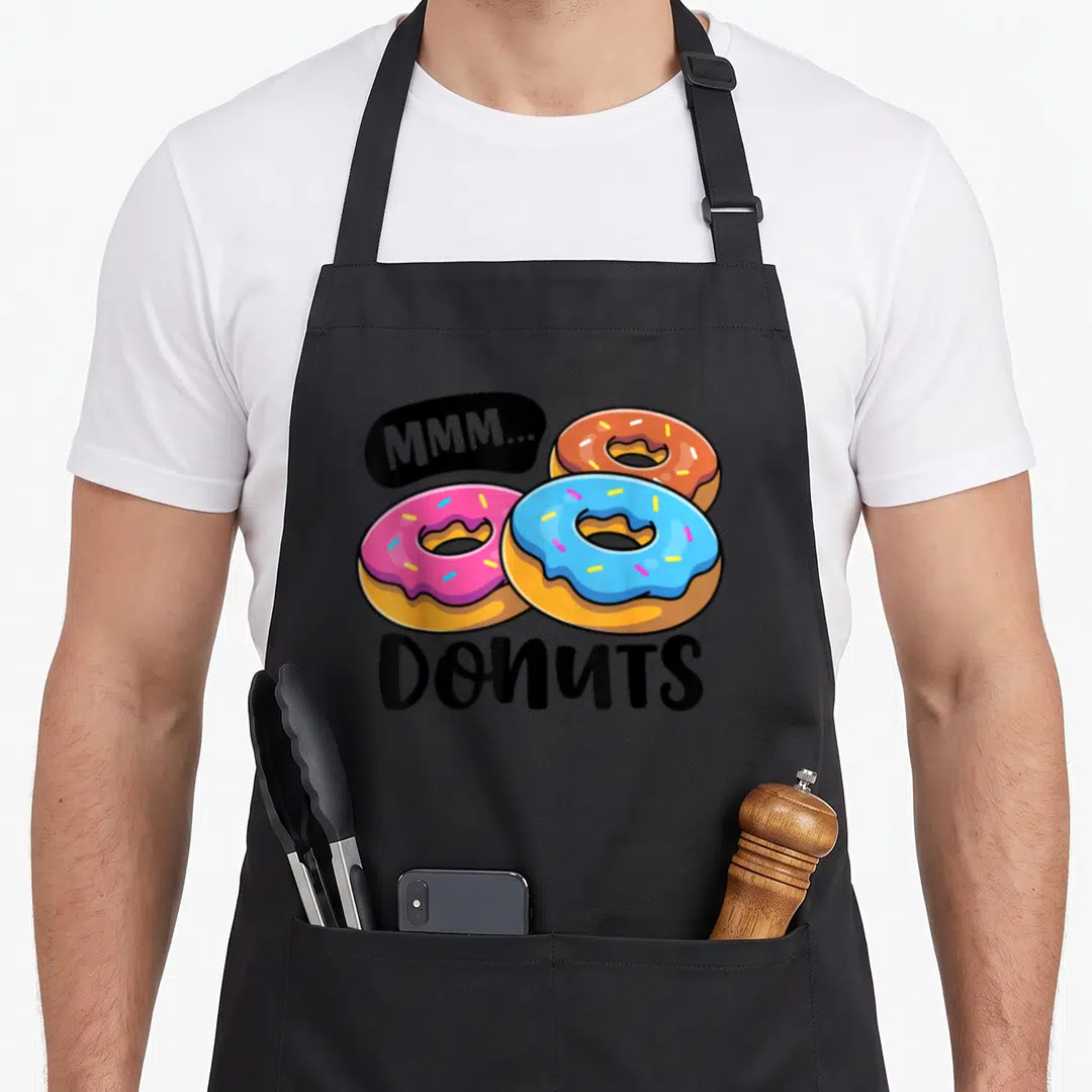 Mmm food aprons - Three pink blue and brown donuts with MMM... Donuts text in cartoon style — shown on a black cotton canvas apron against a white background