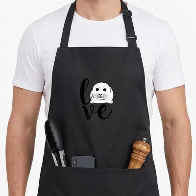 Baby harp apron - Cartoon seal head replacing the letter O in the word love printed in black script — shown on a black cotton canvas apron against a white background