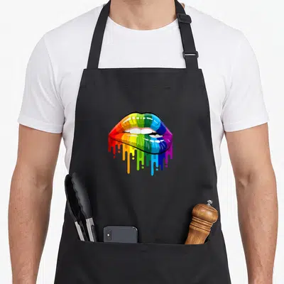 Bite rainbow apron - Pair of rainbow lips with white teeth and colorful paint dripping down — shown on a black cotton canvas apron against a white background