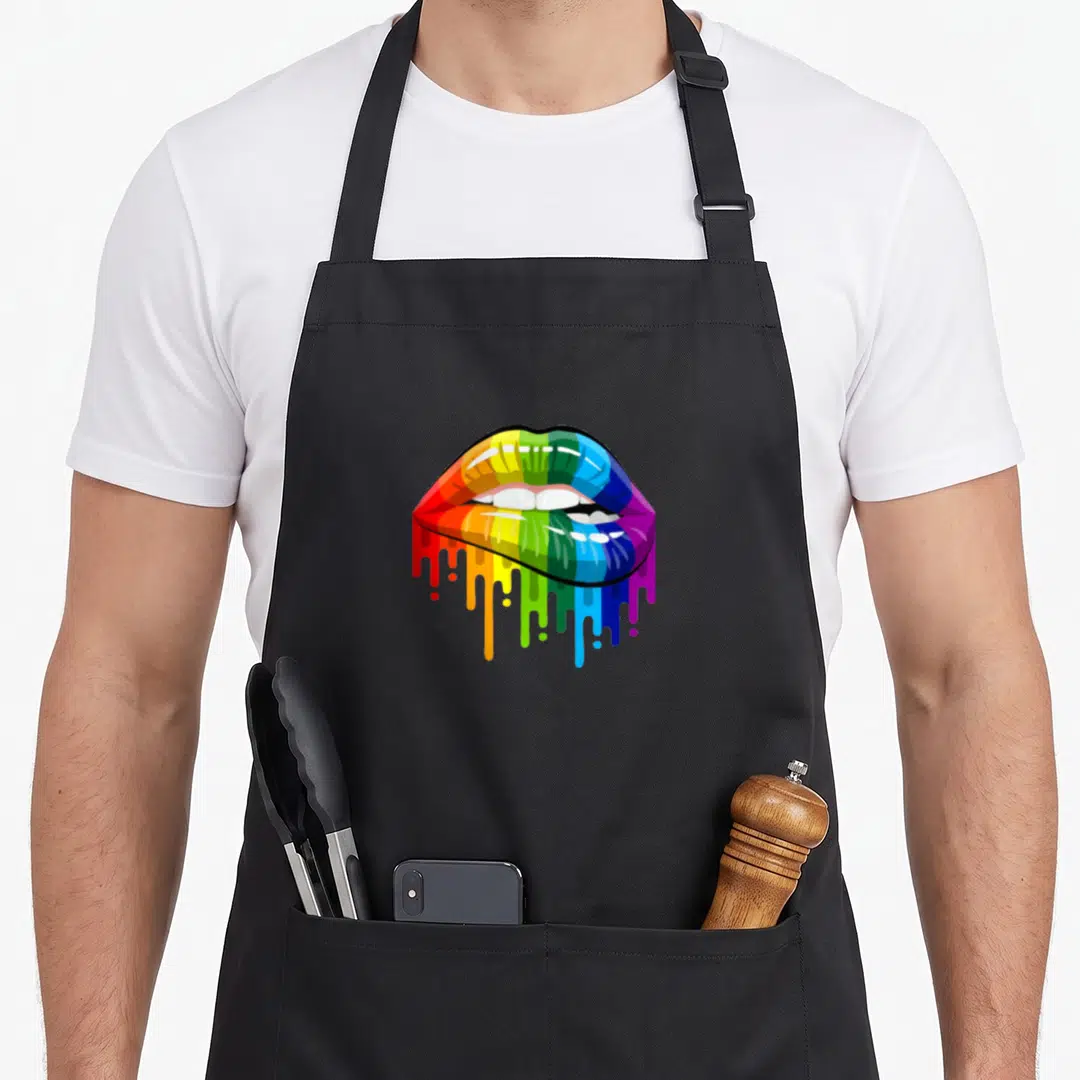 Bite rainbow apron - Pair of rainbow lips with white teeth and colorful paint dripping down — shown on a black cotton canvas apron against a white background