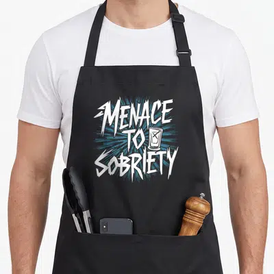 Addiction alcohol recovery apron - White jagged MENACE TO SOBRIETY text with crossed-out glass on blue burst background — shown on a black cotton canvas apron against a white background