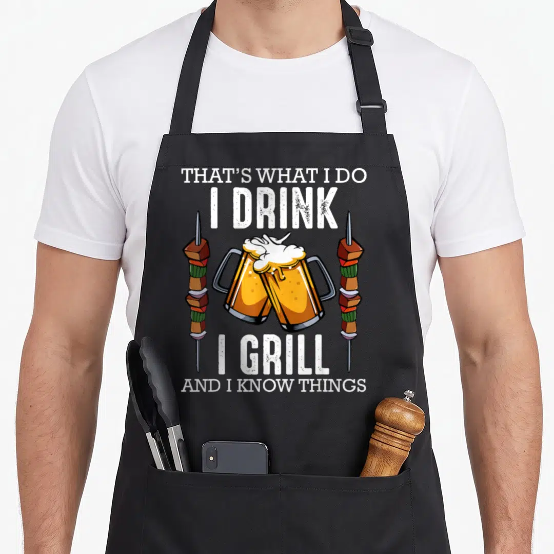 Drink speck apron - Two beer mugs toasting between vertical shish kebabs with stacked white text above and below — shown on a black cotton canvas apron against a white background