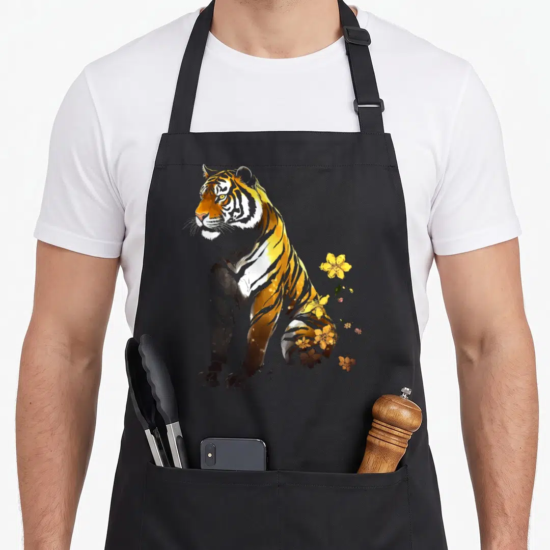 Artwork flower animal apron - Seated tiger in watercolor with yellow flowers and black stripes on black bib — shown on a black cotton canvas apron against a white background