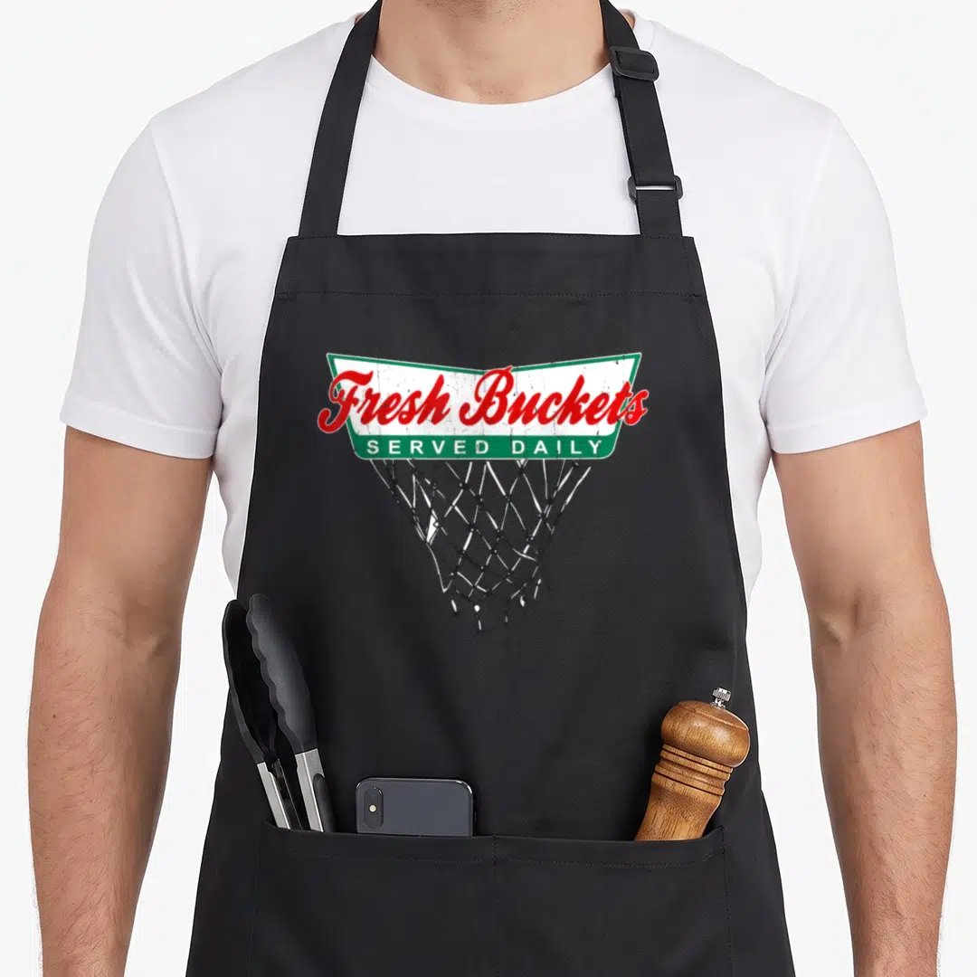 Basketball bucket apron - Fresh Buckets Served Daily banner over basketball net in red green and black — shown on a black cotton canvas apron against a white background