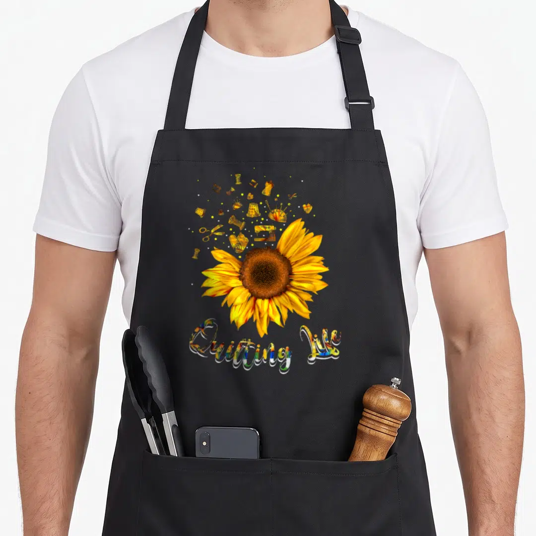 Sun quilting apron - Realistic sunflower with yellow sewing tools and Quitting My text — shown on a black cotton canvas apron against a white background