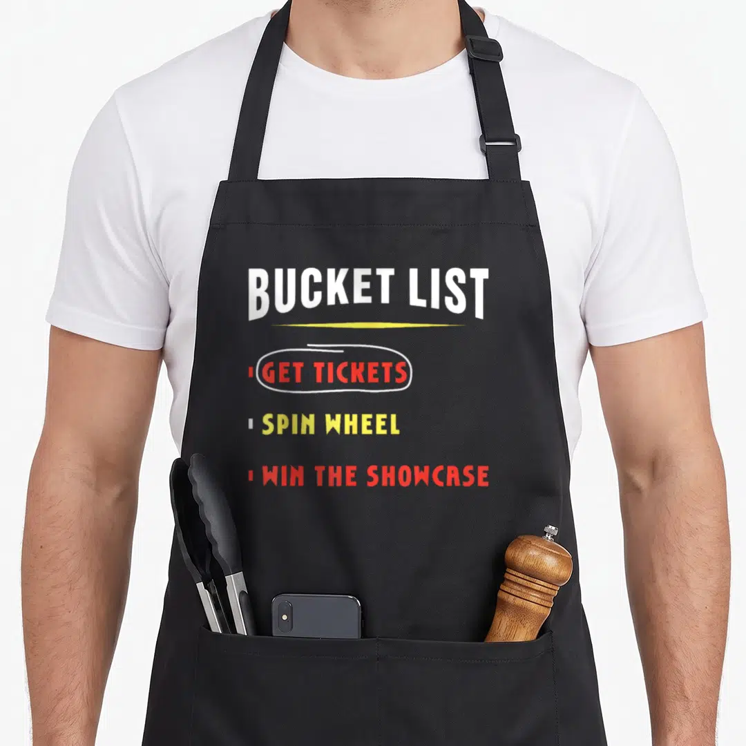 Game bucket apron - Stacked BUCKET LIST text with GET TICKETS in oval, SPIN WHEEL, WIN THE SHOWCASE in red yellow white — shown on a black cotton canvas apron against a white background