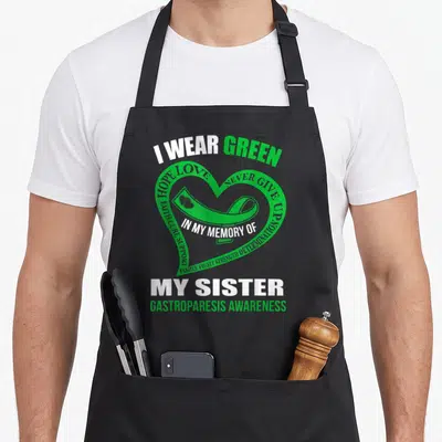 Gastroparesis memory apron - Green heart with ribbon and text I WEAR GREEN MY SISTER GASTROPARESIS AWARENESS — shown on a black cotton canvas apron against a white background