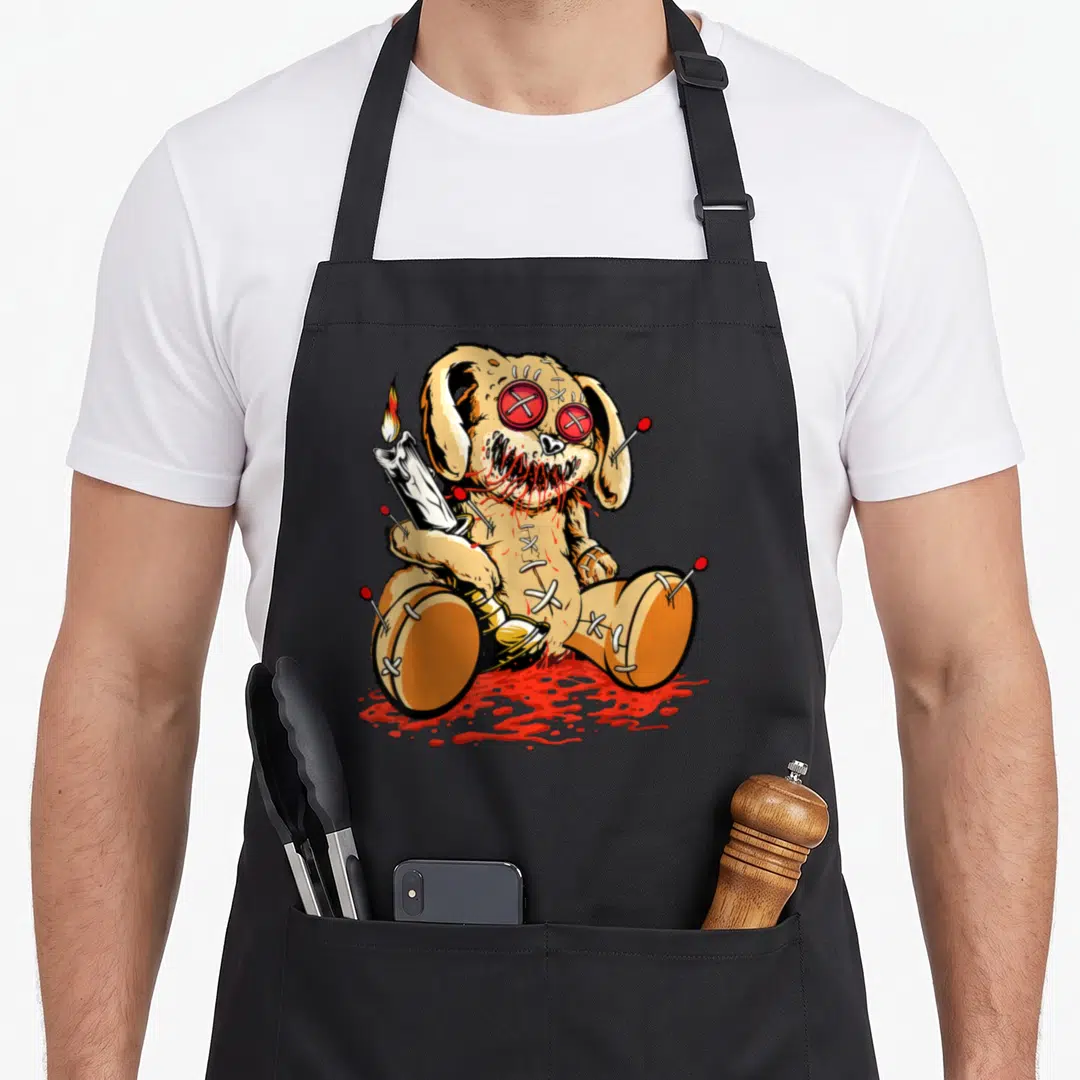 Voodoo teddy bear apron - Tan cartoon voodoo doll with red pins holding white candle in red pool — shown on a black cotton canvas apron against a white background