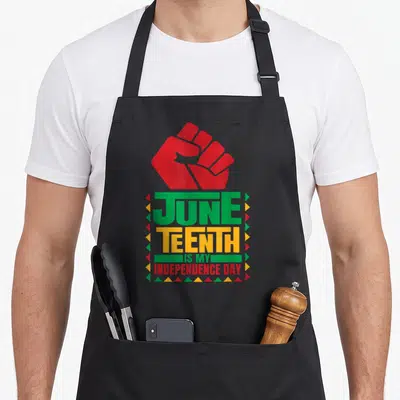 Juneteenth galveston apron - Red raised fist above stacked text JUNE TEENTH IS MY INDEPENDENCE DAY bordered by colored — shown on a black cotton canvas apron against a white background