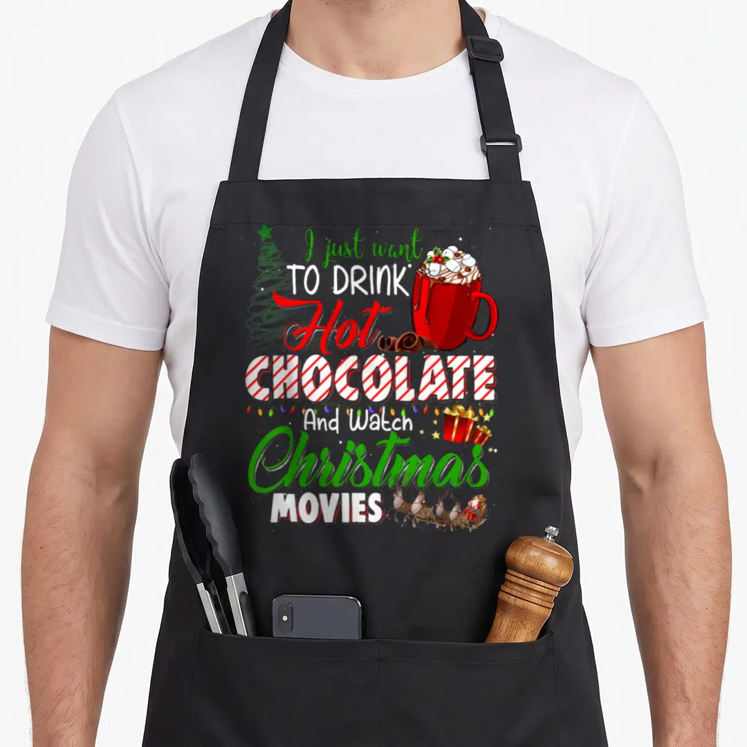 Chocolate watch the christmas apron - Stacked text reading I just want to drink hot chocolate next to a red mug — shown on a black cotton canvas apron against a white background