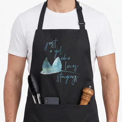 Shark stingray apron - Watercolor stingray in blue and teal with vertical cursive text reading just a girl who loves — shown on a black cotton canvas apron against a white background