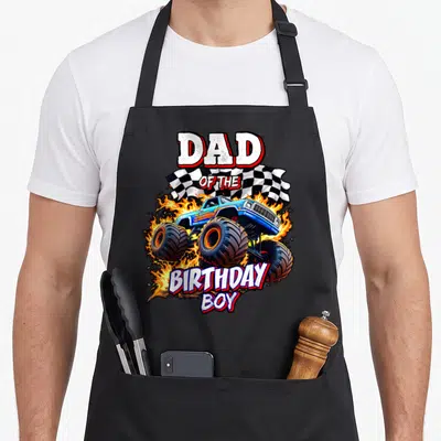 Retro birthday truck apron - DAD OF THE BIRTHDAY BOY text over blue monster truck with flames and checkered flag — shown on a black cotton canvas apron against a white background