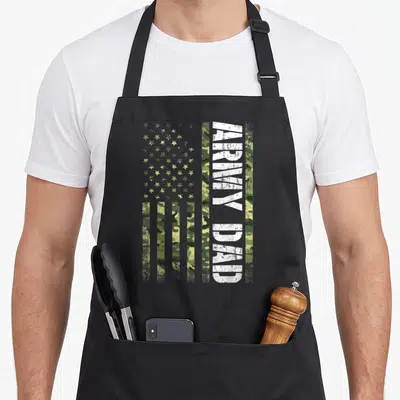 State father day apron - Vertical ARMY DAD text on camouflage US flag with distressed white lettering — shown on a black cotton canvas apron against a white background