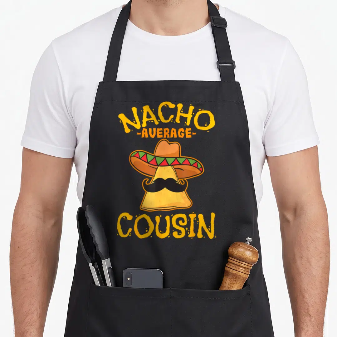 Cousin mexican apron - Cartoon nacho chip in sombrero with mustache and stacked yellow text NACHO AVERAGE COUSIN — shown on a black cotton canvas apron against a white background
