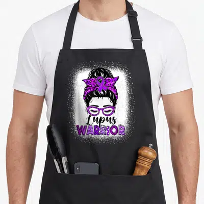 Lupus messy aprons - Cartoon woman bun glasses purple leopard print ribbon Lupus WARRIOR text — shown on a black cotton canvas apron against a white background