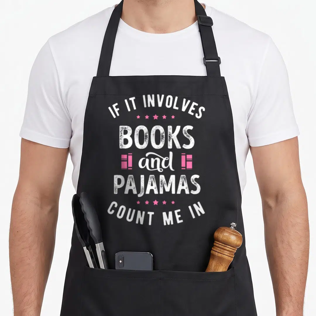 Involve nerd apron - Stacked text IF IT INVOLVES BOOKS and PAJAMAS COUNT ME IN with pink books and stars — shown on a black cotton canvas apron against a white background