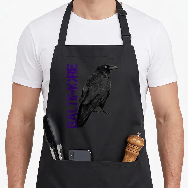 Maryland baltimore ravens apron - Realistic black crow illustration next to vertical purple BALTIMORE text — shown on a black cotton canvas apron against a white background