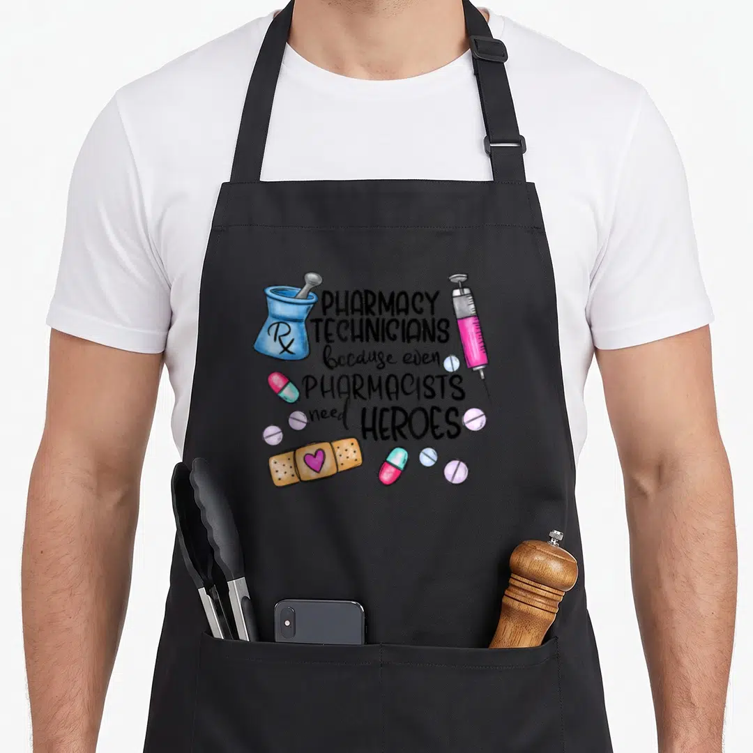 Cpht pharmacist apron - Cartoon pharmacy tools with text PHARMACY TECHNICIANS because even PHARMACISTS need HEROES — shown on a black cotton canvas apron against a white background