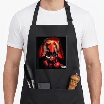 Revenge general apron - Darth Vader helmet reflection of two lightsaber fighters with Star Wars text — shown on a black cotton canvas apron against a white background