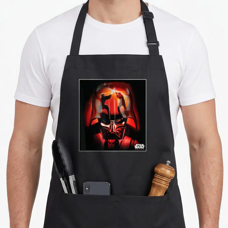 Revenge general apron - Darth Vader helmet reflection of two lightsaber fighters with Star Wars text — shown on a black cotton canvas apron against a white background