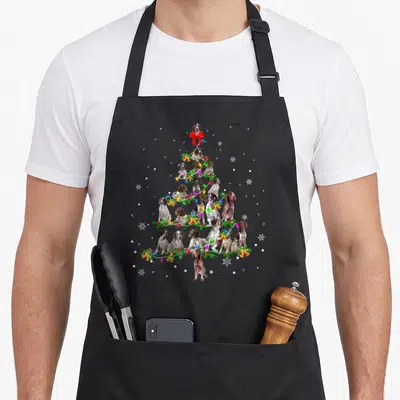 Shorthaired christmas tree apron - Triangle of brown and white dogs forms Christmas tree with red bow, lights, bells — shown on a black cotton canvas apron against a white background