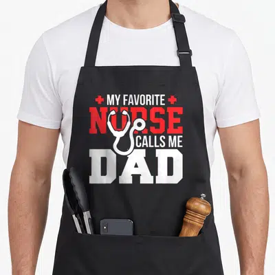 Call father nurses apron - White stethoscope over red and white text MY FAVORITE NURSE CALLS ME DAD flanked by two red — shown on a black cotton canvas apron against a white background