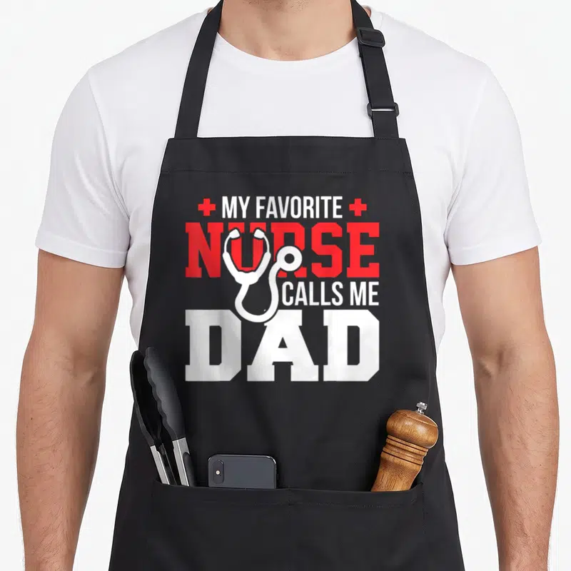 Call father nurses apron - White stethoscope over red and white text MY FAVORITE NURSE CALLS ME DAD flanked by two red — shown on a black cotton canvas apron against a white background