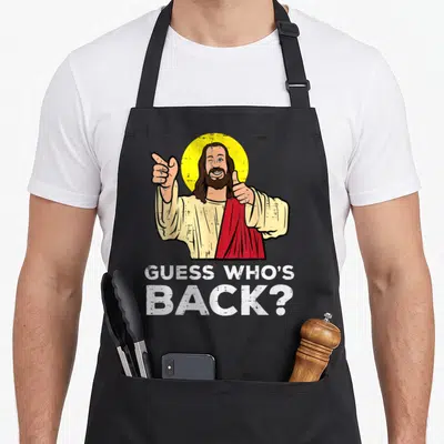Guess easter apron - Cartoon Jesus thumbs up GUESS WHO'S BACK? text yellow red cream white — shown on a black cotton canvas apron against a white background