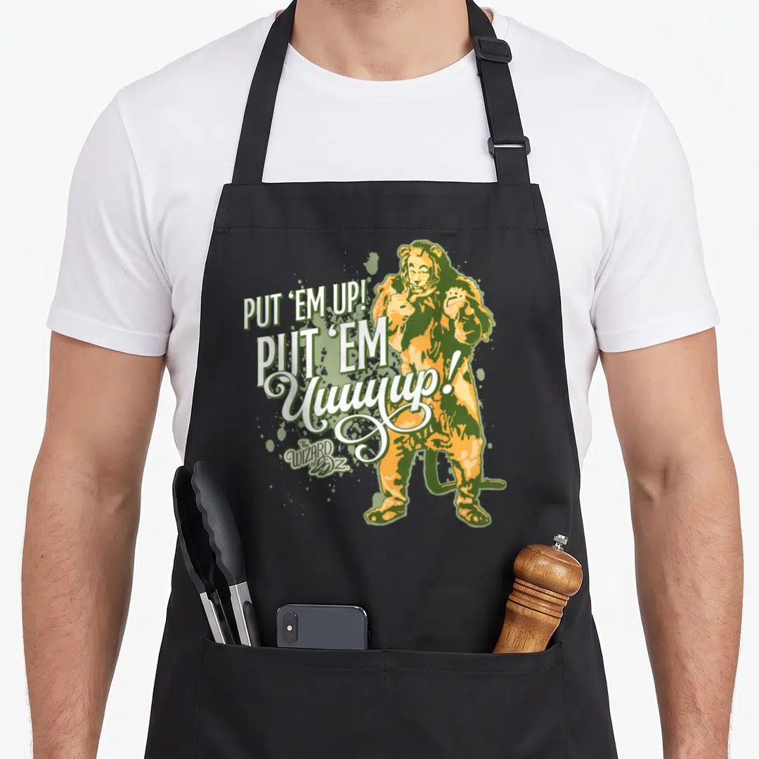 Wizard lion apron - Cowardly Lion in orange and green with stacked PUT EM UP text and Wizard of Oz logo — shown on a black cotton canvas apron against a white background